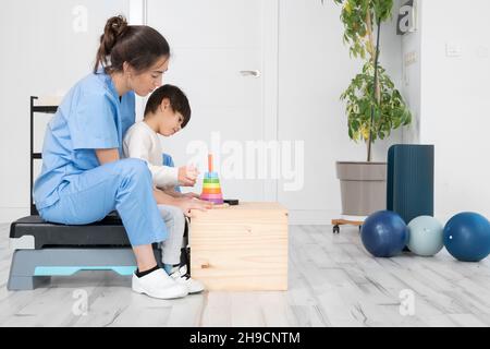 Therapeut tun Entwicklungsaktivitäten mit einem kleinen Jungen mit zerebraler Lähmung, mit Rehabilitation, Lernen . Ausbildung im medizinischen Versorgungszentrum. Hochwertige Fotos. Stockfoto