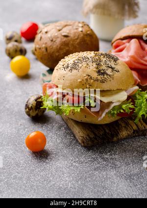 Köstliches knuspriges Burger-Brötchen mit geschnittenem Schinken auf einem alten Holzschneidebrett. Dunkel launisch Essen Stillleben. Stockfoto