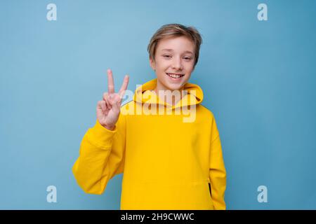 Porträt eines attraktiven jungen Mannes, der verschiedene Handgesten auf einer leeren Werbefläche im gelben Sweatshirt zeigt, isoliert auf blauem Hintergrund Stockfoto