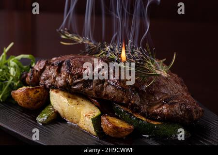 Gegrilltes Striploin-Steak auf schwarzer Platte. Steak mit gebratenen Kartoffeln und Gemüse Stockfoto