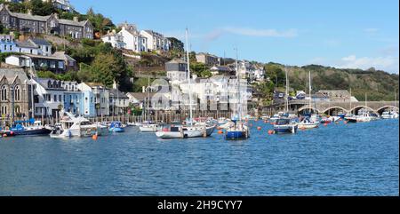 Der Hafen in Looe Cornwall zeigt die Wohnungen auf den Hügeln, die die vielen auf dem Wasser verankerten Boote und die Brücke umgeben Stockfoto