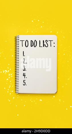 Spiralnotizbuch mit To-do-Liste auf hellgelbem Hintergrund mit verschwommenem Licht Bokeh, Draufsicht, flaches Lay Stockfoto