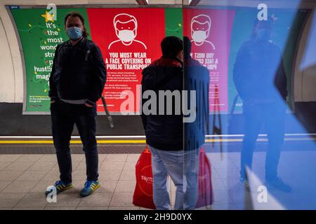 London, Großbritannien. 6. Dezember 2021. Pendler passieren ein Schild an der U-Bahnstation Oxford Circus, in dem die Fahrgäste im öffentlichen Nahverkehr eine Gesichtsbedeckung tragen müssen. Nach der Entdeckung der Omicron-Variante hat die britische Regierung das Tragen von Gesichtsbezügen im öffentlichen Verkehr und in Geschäften obligatorisch gemacht. Eine Minderheit von Passagieren und Käufern weigert sich, die Einhaltung zu gewährleisten, obwohl Geldstrafen verhängt werden können und die Durchsetzung von Vorschriften von einigen Parteien als schwierig angesehen wird. Kredit: Stephen Chung / Alamy Live Nachrichten Stockfoto