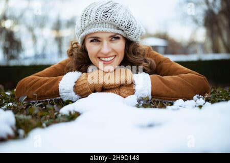 Happy Modern 40 Jahre alte Frau mit Fäustlingen in einem Strickhut und Schaffell Mantel im Freien im Stadtpark im Winter. Stockfoto