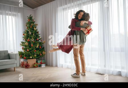 Frohe Feiertage. Liebevolles Paar, das in der Nähe des Weihnachtsbaums zu Hause Geschenke austauscht. Stockfoto