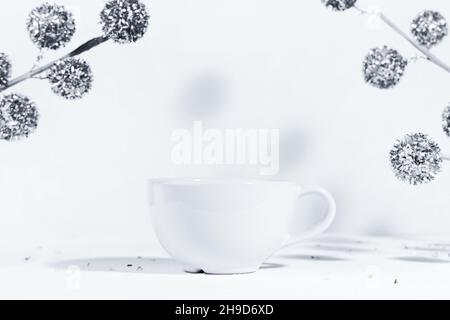 Weihnachtlicher Hintergrund mit einem weißen Keramikbecher mit einem Wintergetränk, auf einem weißen Hintergrund mit weihnachtlichen Dekorationen und harten Schatten in der Sonne. Stockfoto