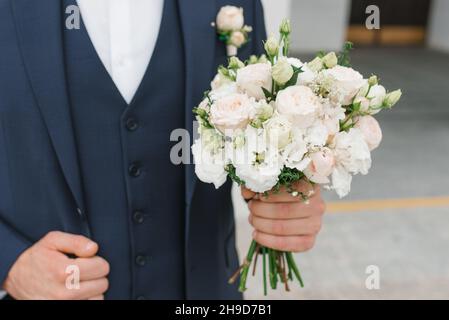 Der Bräutigam im blauen Anzug hält in der Hand einen zarten Brautstrauß für seine geliebte Braut Stockfoto