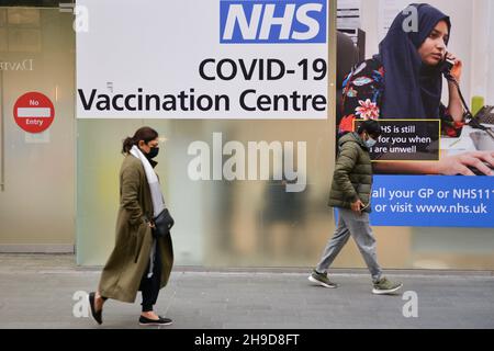 Fußgänger, die am NHS Covid-19 Impfzentrum in Westfield, Stratford, vorbeikommen. Das Vereinigte Königreich führt Pandemiebeschränkungen wieder ein, während die Omicron COVID-19-Variante auftaucht. Booster-Jabs werden im Januar erhältlich sein. Stockfoto