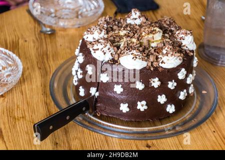 Schokoladenkuchen mit Schlagsahne und Bananen wird geschnitten Stockfoto