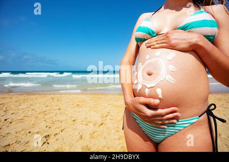 Sonnencreme auf den Bauch einer Schwangeren Stockfoto