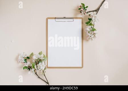 Leeres Blatt Papier Notizblock mit Clip, Apfelbaum Äste mit Blumen auf beigem Hintergrund. Ein minimaler Desktop für das Home Office. Flach liegend, Draufsicht. Stockfoto