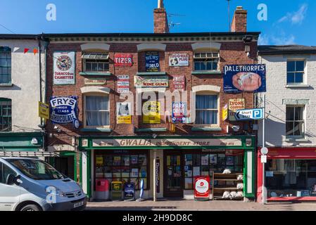 Der Gwalia Convenience Store in Broad Street, Ross-on-Wye, Herefordshire, ist mit zahlreichen alten Vintage-Werbeschilder an der Außenwand dekoriert Stockfoto