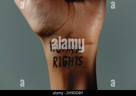Nahaufnahme des Handgelenks eines Mannes mit dem darin geschriebenen Text Menschenrechte auf grauem Hintergrund Stockfoto