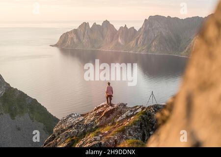 Fotograf mit Stativ, der den Sonnenuntergang vom Husfjellet-Gipfel, Senja Island, Troms County, Norwegen, beobachtet Stockfoto