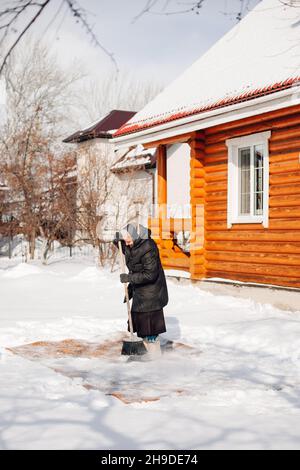 Seitenansicht der Frau, die den Teppich putzte. Kaukasische Frau reinigt Teppich mit traditionellen Methoden der ökologischen Reinigung mit Neuschnee und Besen in der Nähe von Holz Stockfoto