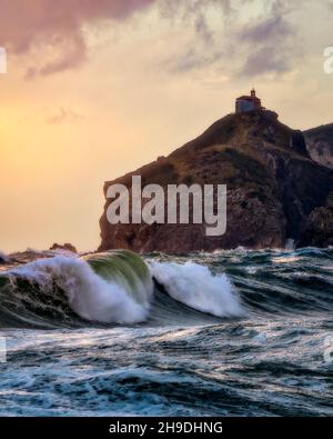 atardecer sobre san juan de gaztelugatxe, con una bonita ola, la perspectiva desde una de las playas de bacio, en una tarde noviembre Stockfoto