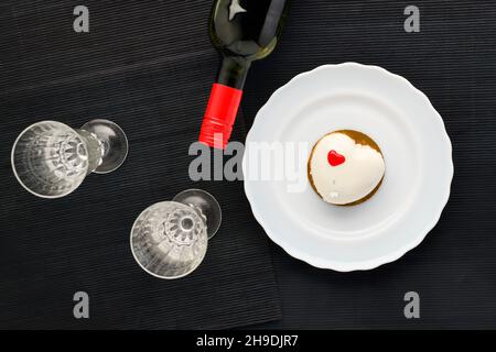 Ein Kuchen in Herzform. Mousse Cupcake in Herzform auf schwarzem Hintergrund mit zwei Gläsern und einer Flasche Rotwein. Valentinstag. Stockfoto