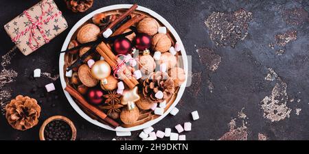 Nüsse und weihnachtliche Gewürze in Keramikschale auf dunklem Schiefer-, Stein- oder Metallhintergrund. Kulinarischer Hintergrund mit Zutaten zum Backen von Schokoladenkeksen Stockfoto