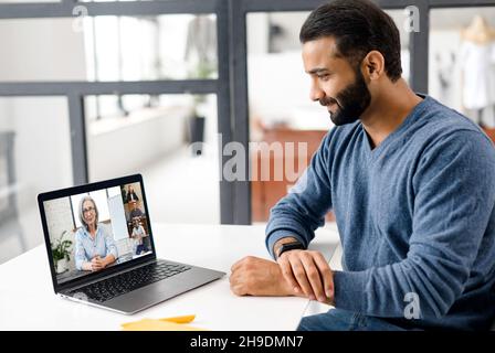 Indischer Student, der online studiert, ein Webinar mit einer Lehrerin ansieht und andere Studenten daran beteiligt ist. Ethnischer, multirassischer Mann, Mitglied einer Videokonferenz, der einen Laptop für die Online-Verbindung verwendet Stockfoto