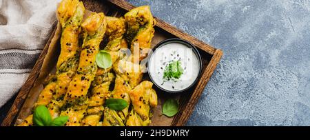 Hausgemachte Brotstäbchen mit Käse, Pesto-Sauce und schwarzen Sesamkörnern auf grauem Stein im Vintage-Hintergrund. Draufsicht. Stockfoto