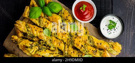Hausgemachte Brotstäbchen mit Käse, Pesto-Sauce und schwarzen Sesamkörnern auf grauem Stein im Vintage-Hintergrund. Draufsicht. Stockfoto