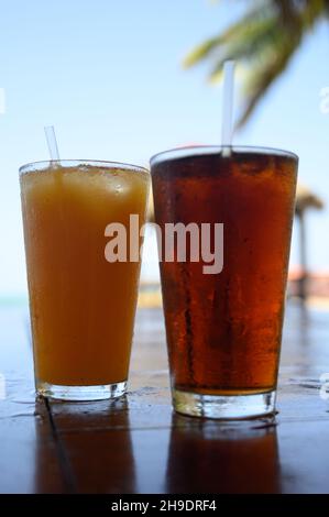 Das Foto zeigt Coca Cola Erfrischungen und Passionsfruchtsaft. Foto aufgenommen in der Bar auf einer karibischen Insel. Der Strand und die Meereslinie sind in der sichtbar Stockfoto