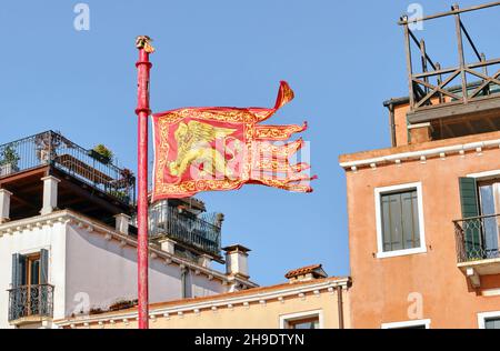 Flagge Venedigs im Hintergrund der traditionellen italienischen Architektur, das wichtigste venezianische Symbol, der goldene geflügelte Löwe des Evangelisten Markus Stockfoto