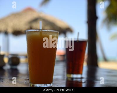 Das Foto zeigt Coca Cola Erfrischungen und Passionsfruchtsaft. Foto aufgenommen in der Bar auf einer karibischen Insel. Der Strand und die Meereslinie sind in der sichtbar Stockfoto