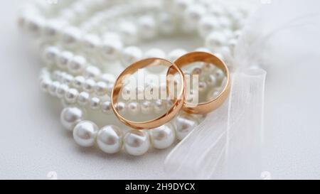 Eheringe und Perlenarmband auf weißem Hintergrund. Brautzubehör aus nächster Nähe. Klassische Hochzeit goldenen Bands. Stockfoto