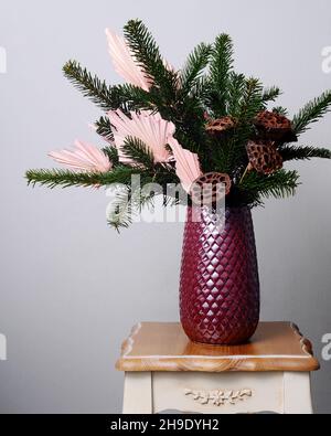 Winterstrauß mit Kiefernzweigen und getrocknetem Lotus in einer violetten Vase. Blumendekor mit getrockneten Blumen. Stockfoto