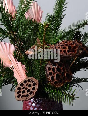 Winterstrauß mit Kiefernzweigen und getrocknetem Lotus in einer violetten Vase. Blumendekor mit getrockneten Blumen in Nahaufnahme. Stockfoto