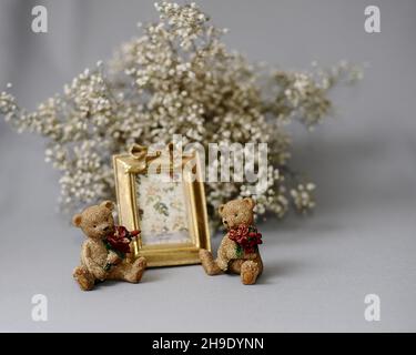 Geschenkidee zum Valentinstag. Goldener Fotorahmen und Figuren von Teddybären mit roten Blumensträußen. Niedliches Geschenk-Konzept. Stockfoto