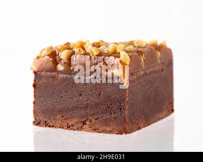 Schokoladen-Brownie-Kuchenstück isoliert auf weiß. Biss Größe feuchte braune Schokolade Brownie mit Karamell und Erdnuss Belag, isoliert auf weißem Hintergrund mit Clipping Pfad. Stockfoto