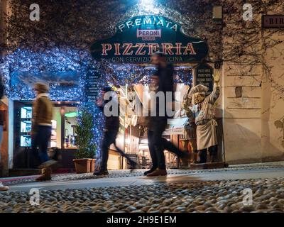 Mailand, Lombardei, Italien. Dezember 2019. Menschen, die nachts vor der façade einer typisch italienischen Pizzeria in Mailand vorbeikommen. Stockfoto