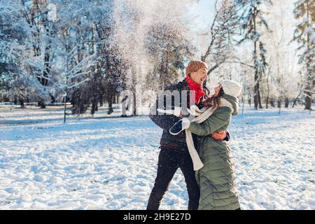 Glückliches junges, liebevolles Paar, das mit Schnee spielt, der ihn im Winterpark wirft. Mann und Frau haben Spaß im Freien. Stockfoto
