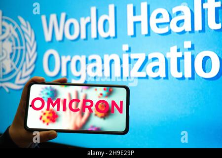 Handliches Mobiltelefon mit omicron COVID 19-Variantenstamm vor der Flagge der WHO, die Nachrichten-App-Benachrichtigungen anzeigt Stockfoto