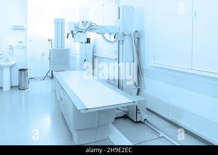 Röntgenabteilung im modernen Krankenhaus. Röntgenraum mit Scangerät und leerem Bett. Techniker, der ein Röntgengerät anpasst. Scannen von Brust, Herz Stockfoto