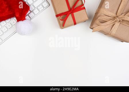 Flat Lay Weihnachtskonzept. Eine Computertastatur mit Weihnachtsmütze und zwei in Normalpapier verpackten Geschenken und Platz zum Kopieren in der unteren Hälfte des Bildes. Stockfoto