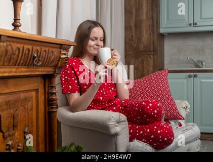 Frau mit Teetasse und Keks in den Händen, sitzend in einem gemütlichen Zuhause in den Winterferien. Stockfoto