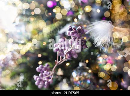 Weihnachtshintergrund mit verschwommenem Bokeh von Weihnachten glühenden Lichtern und Tannenzweig mit violetten Beeren. Stockfoto