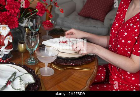 Der Esstisch ist für ein festliches Abendessen im Winter mit den Händen dekoriert und dekoriert. Nahaufnahme von weißer Serviette und roten Beeren zu Weihnachten und Neujahr. Stockfoto