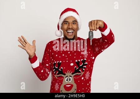 Aufgeregt schwarz Kerl in Santa Hut hält Schlüssel aus Auto Stockfoto