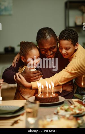 Vertikales Porträt eines glücklichen afroamerikanischen Mannes, der Kinder umarmt, während er mit der Familie Geburtstag feiert Stockfoto