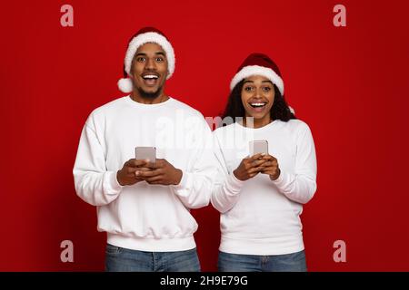 Schöne schwarze Paar in Santa Hüte mit Smartphones Stockfoto