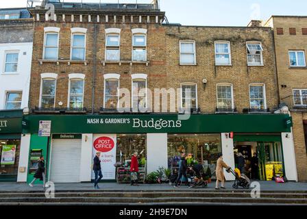 Nash und Gardener's Budgens Supermarkt mit Postamt mit Leuten, die an der Upper Street London Borough of Islington vorbeikommen Stockfoto