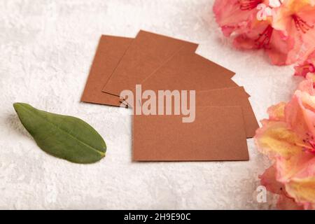 Braune Visitenkarte mit rosa Azaleen-Blüten auf grauem Beton-Hintergrund. Seitenansicht, Kopierraum, Modell, Vorlage, Frühling, Sommer-Minimalismus-Konzept. Stockfoto