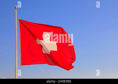 Die Flagge der Schweiz befindet sich auf dem Mast und dort winkt sie im Wind und ist am blauen Himmel sichtbar. Stockfoto