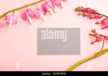 Graue Visitenkarte mit rosa dicentra, gebrochene Herzblumen auf rosa pastellfarbenem Hintergrund. Draufsicht, flaches Lay, Kopierraum, Mockup, Vorlage, Spring, summe Stockfoto