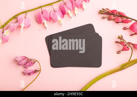 Schwarze Visitenkarte mit rosa dicentra, gebrochene Herzblumen auf rosa pastellfarbenem Hintergrund. Draufsicht, flaches Lay, Kopierraum, Mockup, Vorlage, Feder, Summ Stockfoto