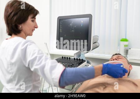 Arzt, der eine doppler-Sonographie bei einem männlichen Patienten in einer Kardiologieklinik macht. Kardiologe, der eine Ultraschalluntersuchung am Herz-Kreislauf-System durchführt Stockfoto